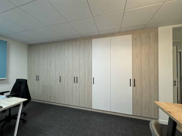 Grandes armoires sur mesure en bois clair et blanc avec poignées noires, offrant un rangement optimisé dans un bureau professionnel moderne et épuré.