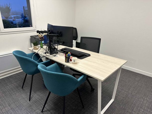 Bureau sur mesure avec un plateau en bois clair, équipé d'écrans doubles sur support, fauteuils bleus confortables, et des éléments de décoration minimaliste, dans un espace de travail lumineux.